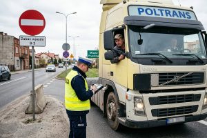 Policjant wręcza mandat kierowcy ciężarówki przy znaku zakazu wjazdu B-2 na granicy miasta